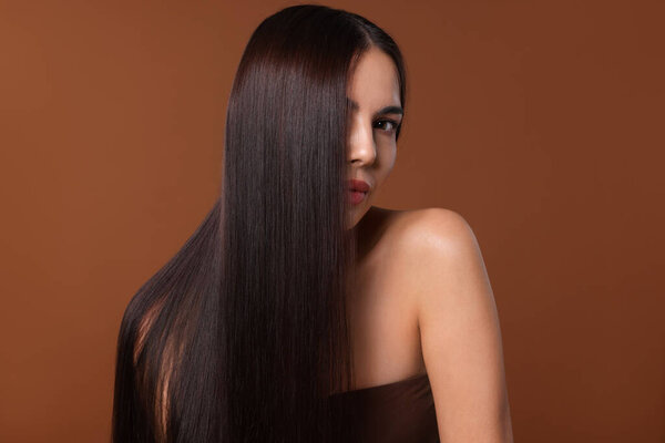 Woman with beautiful smooth hair after lamination procedure on brown background