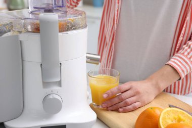 Kadın, modern meyve sıkacağıyla taze portakal suyu yapıyor.