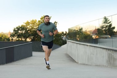 Spor giyimli atletik genç adam dışarıda koşuyor.