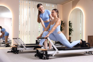 Stüdyoda pilates eğitmeni tarafından yönetilen reformcu kadın üzerinde egzersiz yapıyor.