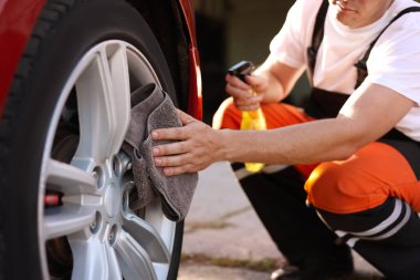 Dışarıdaki gri mikrofiber paçavralarla araba tekerleklerini silen adam, yakın plan.