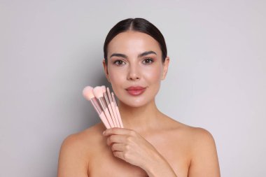 Açık gri arka planda makyaj fırçası olan güzel bir kadın.