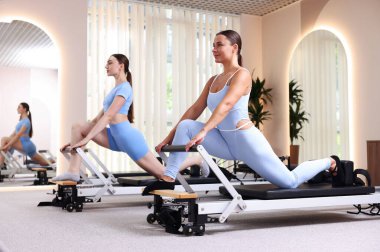 Stüdyoda reformcular üzerinde egzersiz yapan kadın ve pilates eğitmeni.