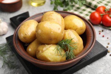 Lezzetli, dereotlu haşlanmış patates, kasede yağ ve gri desenli masada ürünler, yakın plan.