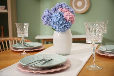 Yemek odasındaki ahşap masada tabaklar ve vazolarla şık bir ortam, yakın plan. İç tasarım