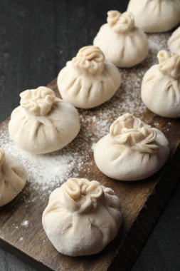 Siyah masa üzerinde un bulunan pişmemiş khinkaliler (hamur tatlısı), yakın plan.