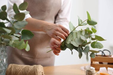 Çiçekçinin ahşap masasında okaliptüs dallarından güzel bir buket yapıyor.