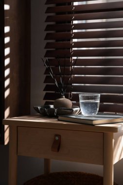 Bir bardak su, defter ve hava sazlığı olan ahşap masa.