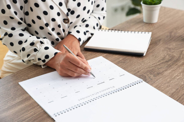 Woman using business planner at wooden table in office, closeup
