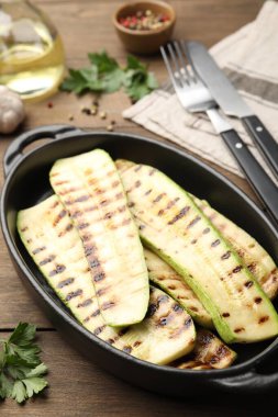 Fırın tabağında lezzetli ızgara kabak dilimleri ve ahşap masada maydanoz, yakın plan.