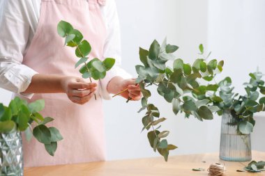 Çiçekçinin ahşap masasında okaliptüs dallarından güzel bir buket yapıyor.