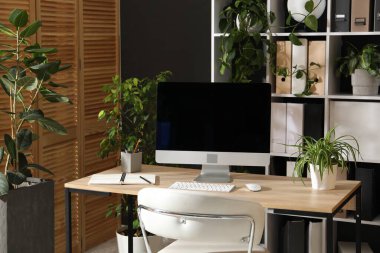 Modern bilgisayarı, kırtasiyesi ve çiçek dekoru olan şık bir iş yeri. Biyofilik iç tasarım