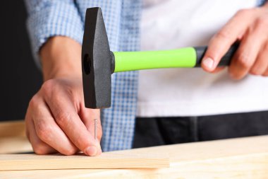 Kapalı alanda tahta çiviye çivi çakan bir adam var.