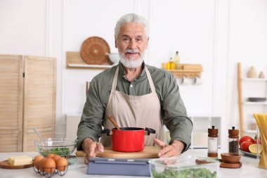 Mutfaktaki beyaz mermer masada yaşlı bir adam yemek pişiriyor.