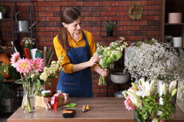 Profesyonel çiçekçi dükkandaki ahşap masada çiçek buketi yapıyor.