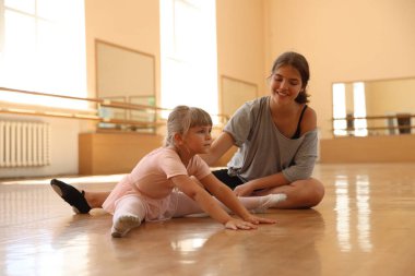 Gülümseyen bale öğretmeni dans dersinde küçük kızın esnemesine yardım ediyor.