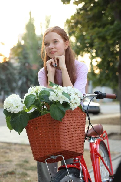Bisikletin yanında güzel bir genç kız ve şehir caddesinde bir sepet çiçek.
