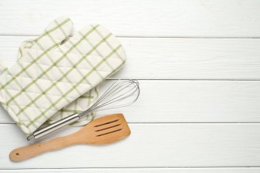 Fırın eldiveni, tutucu, çırpıcı ve spatula beyaz ahşap masa, düz yatak. Metin için boşluk