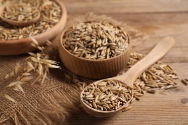 Yulaf taneleri, kaşık, kase ve çuval bezi ahşap masada, yakın plan.