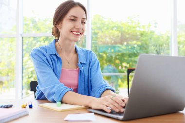 İçerideki ahşap masada dizüstü bilgisayar kullanan kadın. Ev işyeri
