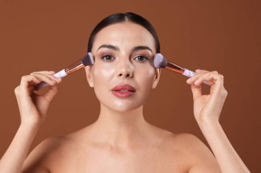Kahverengi arka planda makyaj fırçası olan güzel bir kadın.