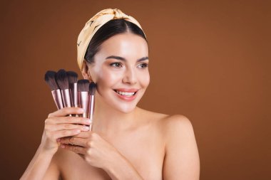 Kahverengi arkaplanda makyaj fırçası olan güzel bir kadın, metin için boşluk