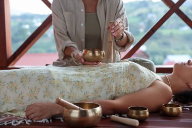 Şarkı söyleyen kadın kase terapisi görüyor. Kapalı yerde yatıyor, yakın plan.