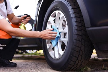 Mavi mikrofiber bez ile araba tekerleklerini silen adam, yakın plan.