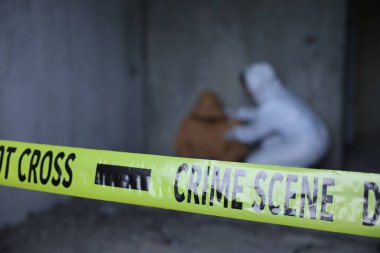 Adli tıp uzmanı terk edilmiş binanın içinde cesetle birlikte olay yerinde çalışıyor. Sarı polis bandına odaklan.