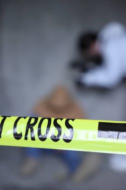 Adli tıp uzmanı terk edilmiş binanın içinde cesetle birlikte olay yerinde çalışıyor. Sarı polis bandına odaklan.