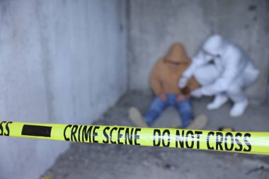 Adli tıp uzmanı terk edilmiş binanın içinde cesetle birlikte olay yerinde çalışıyor. Sarı polis bandına odaklan.