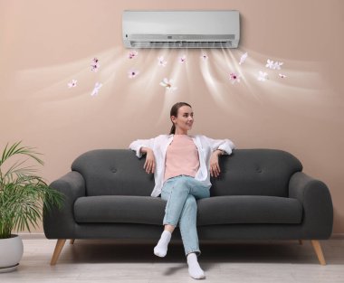 Evdeki kanepede dinlenen gülümseyen kadın. Klima odada rahat bir sıcaklık sağlıyor.