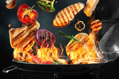 Et ve sebzeler, arka planda mangal ızgarasının üzerinde uçuyor.