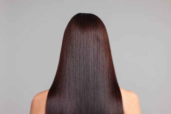 Женщина с красивыми гладкими волосами после процедуры ламинирования на светло-сером фоне, вид сзади
