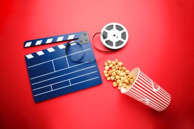 Mavi el çırpma tahtası, film makarası ve kırmızı arka planda patlamış mısır.