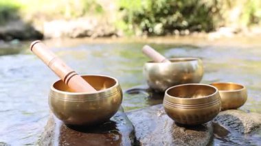 Nehirde taşların üzerinde tokmak olan Tibet müzik kaseleri, yakın plan. Kamera sağa hareket ediyor