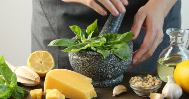 Ahşap masadaki havanda pesto sosu için malzeme ezen kadın, yakın plan.