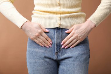 Koyu bej arka planda sistit belirtileri gösteren bir kadın. Yakın plan.