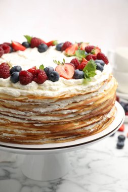 Delicious crepe cake with fresh berries on white marble table, closeup