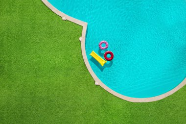 Yüzme havuzunda yüzen şişme halkalar ve şilte yeşil çimlerle çevrili.