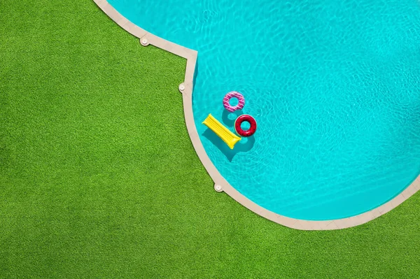 Yüzme havuzunda yüzen şişme halkalar ve şilte yeşil çimlerle çevrili.