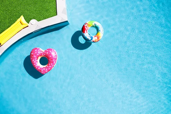 Yeşil çimlerle çevrili yüzme havuzunda yüzen şişme halkalar.