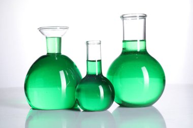 Aynanın yüzeyinde beyaz arka planda yeşil sıvı bulunan farklı bir laboratuar camı.