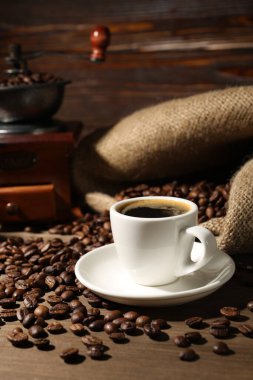 Kahve fincanda, fasulye ve öğütücü ahşap masada.