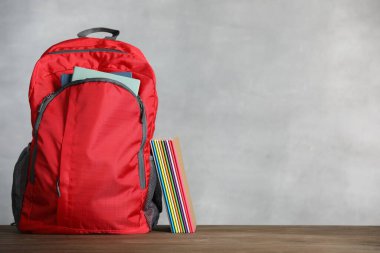 Kırmızı sırt çantası ve defterler gri arka planda tahta masanın üzerinde. Metin için boşluk