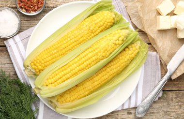 Lezzetli haşlanmış mısır koçanları, ahşap masada dereotu ve baharatlar.