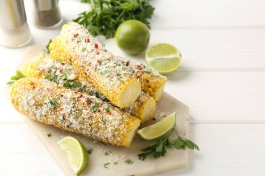 Beyaz ahşap masada maydanozlu, peynirli ve limonlu mısır koçanları.