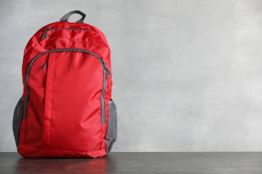 Gri masadaki kırmızı sırt çantası ışık arkaplanı, metin için boşluk