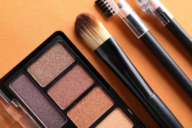 Göz falı paleti ve turuncu arka planda diğer makyaj ürünleri, düz yatış