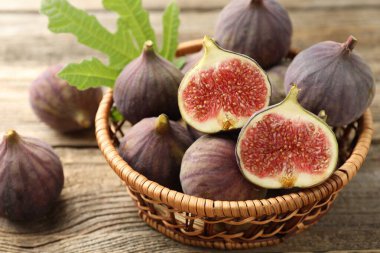 Taze incir ve sepetteki yeşil yaprak ahşap masada, yakın plan.